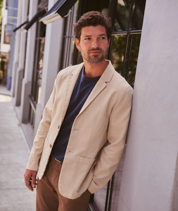 Man wearing Flex Terry Blazer in Dark Khaki leaning against wall, styled with navy tee and brown pants - The Simple Man