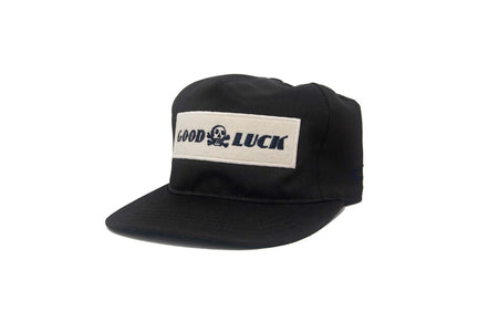 Black Good Luck snapback hat with white felt patch and skull graphic, Ampal unstructured fit, photographed at a front angle for The Simple Man Store.