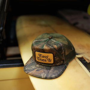 Katin Good Times Trucker Hat in Camo with Easy Does It patch, lifestyle shot on surfboard