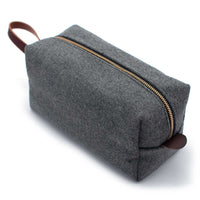Grey Heather Cashmere dopp kit with brass zipper and leather handle, angled top view showing minimalist wool felt design