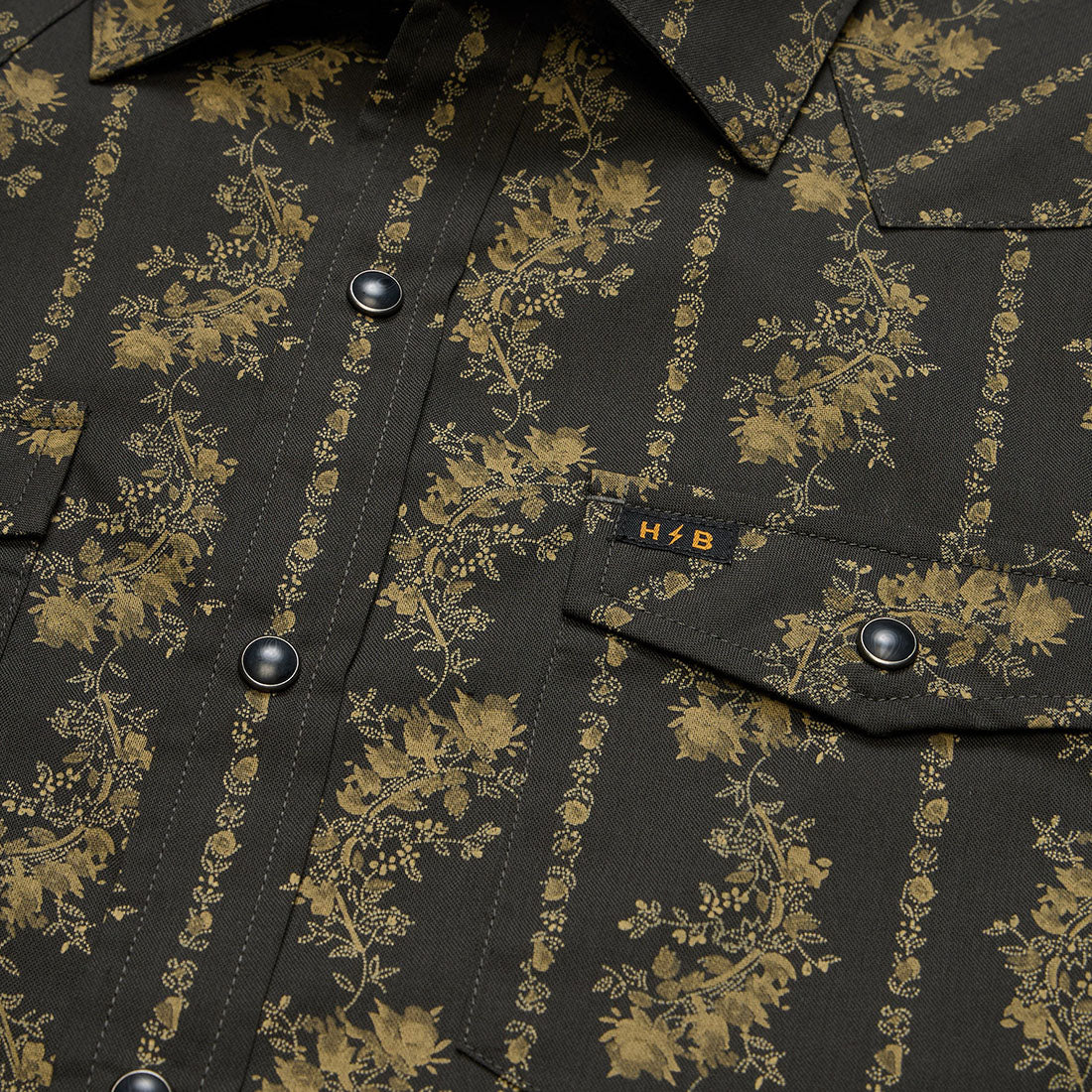 Close-up of pearl snap buttons and woven H/B tag on the black and olive floral stripe Grampa's Curtains H Bar B Snapshirt -- The Simple Man