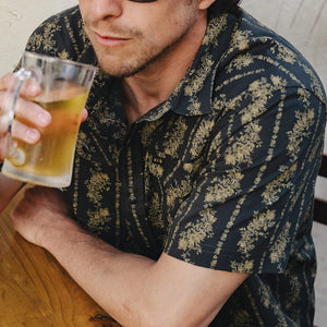 Man drinking a beer while wearing the black and olive floral stripe Grampa's Curtains H Bar B Snapshirt, pearl snap western shirt lifestyle detail -- The Simple Man