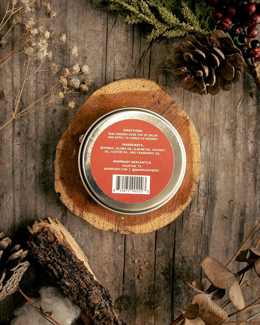 Back of Manready Mercantile Red Label hand salve tin showing ingredients and directions on rustic wood surface