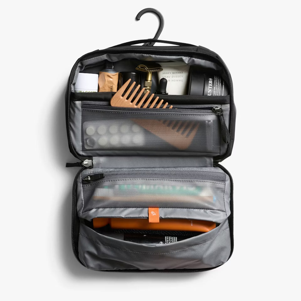 Bellroy black toiletry kit hanging from a rail, displaying upper shelf pocket and lower compartment.