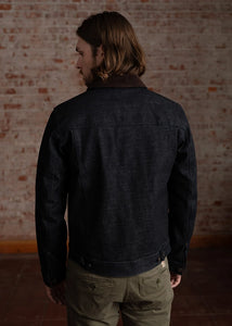 Person wearing a dark denim jacket standing against a brick wall.