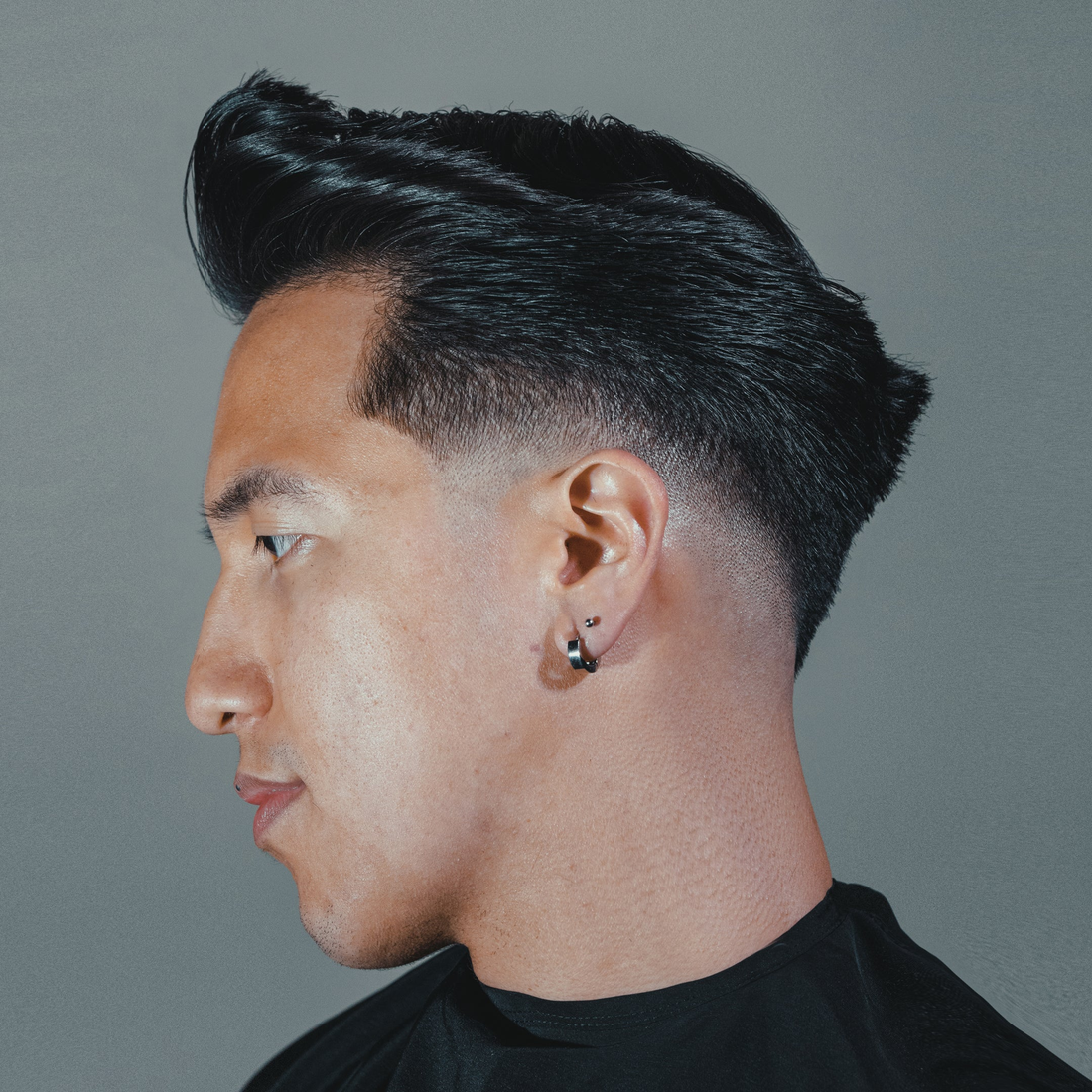 Man in profile with a high slicked-back pompadour and faded sides, styled with Heavymade