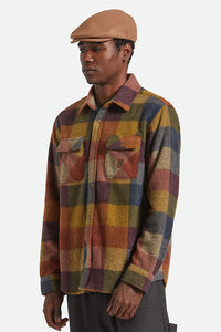 Model wearing the Brixton Hooligan Flat Cap in camel paired with a multicolor plaid shirt.