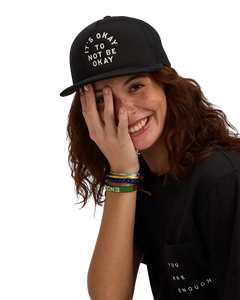 We Are Enough It's Okay Trucker Hat in Real Black front view showing embroidered It's Okay text