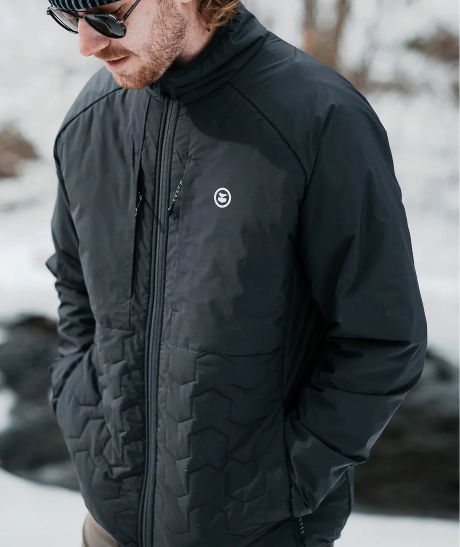 Man wearing the Inlet Puffer Jacket in black near a snowy stream – warm, water-resistant men’s outerwear from The Simple Man Omaha