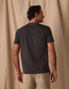 Man wearing The Normal Brand Jersey Henley in Shadow back view – 100% cotton short sleeve henley charcoal gray with chinos warm backdrop