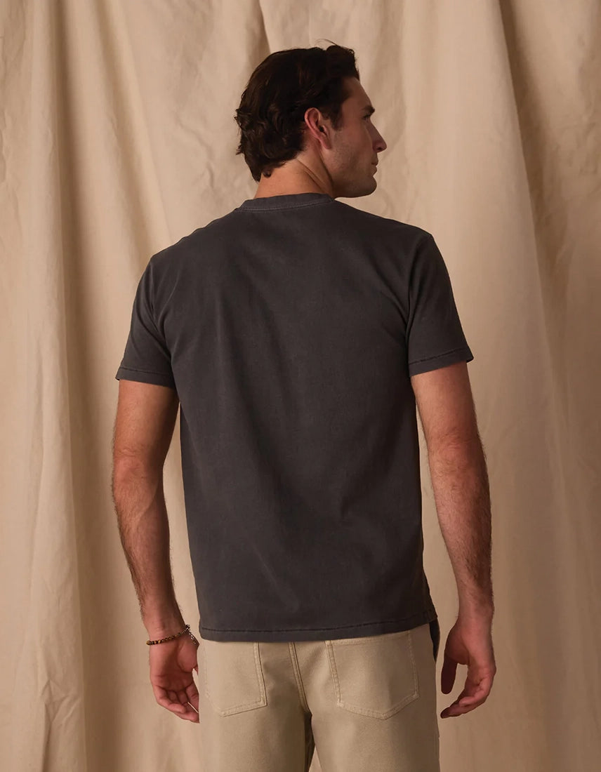 Man wearing The Normal Brand Jersey Henley in Shadow back view – 100% cotton short sleeve henley charcoal gray with chinos warm backdrop