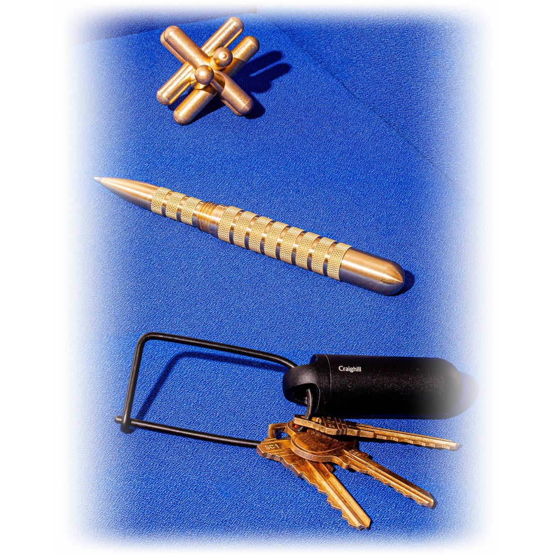 Black Key Capsule on a keyring beside a brass pen and puzzle on a blue surface - The Simple Man