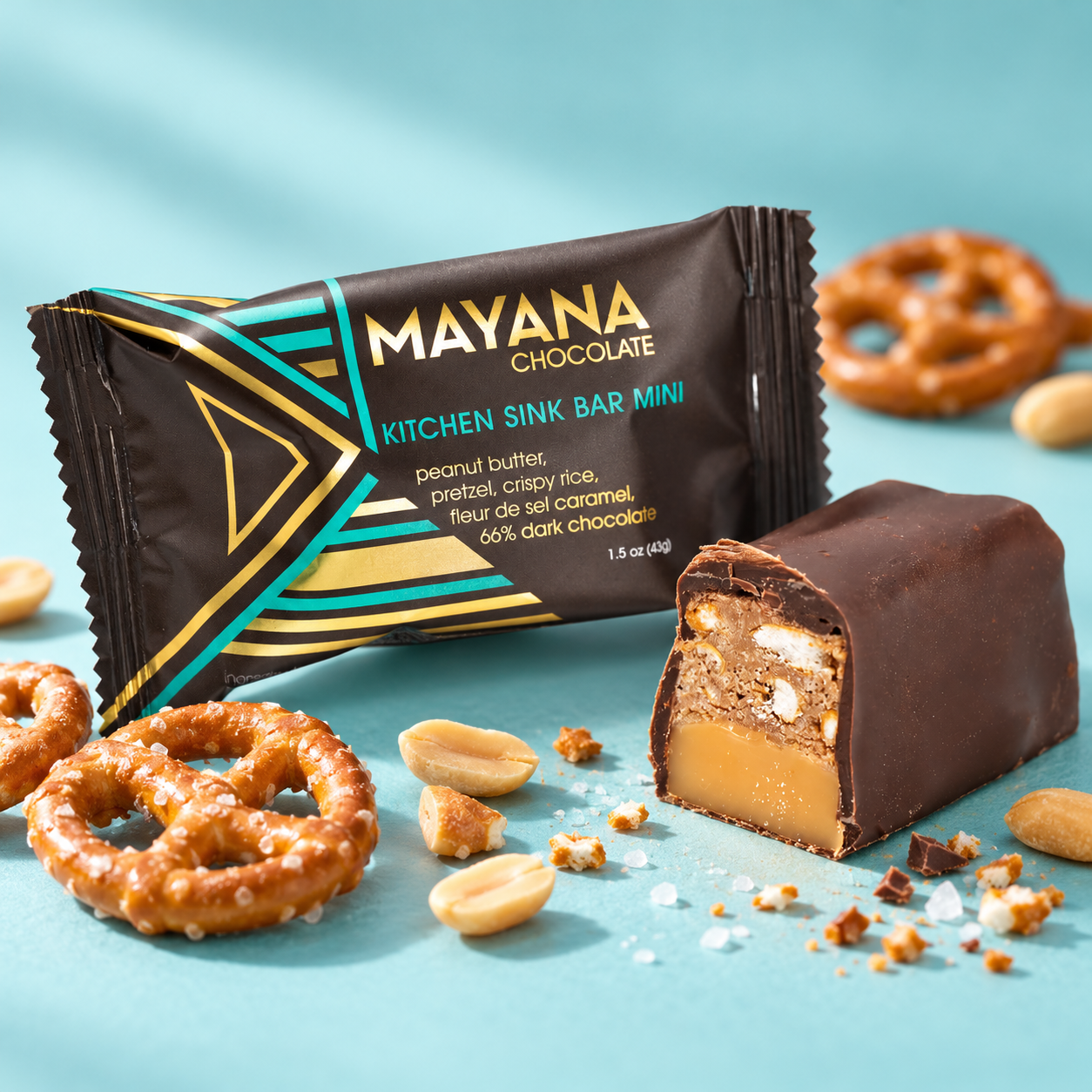 Kitchen Sink mini chocolate bar in its wrapper beside a cut piece showing peanut butter, pretzel and caramel, with pretzels and peanuts around it, The Simple Man