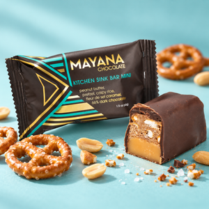 Kitchen Sink mini chocolate bar in its wrapper beside a cut piece showing peanut butter, pretzel and caramel, with pretzels and peanuts around it, The Simple Man