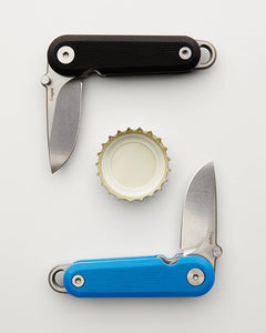Two pocket knives and a bottle cap on a white background