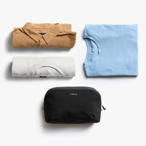 Folded shirts and a black toiletry bag on a white background