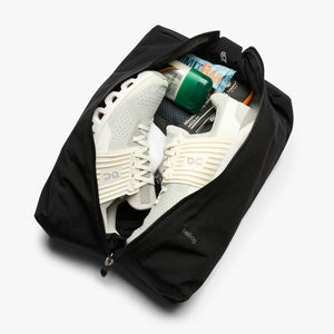 Black travel shoe bag with white sneakers and other items on a white background