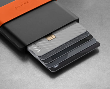 Close-up of cards sliding from The Lowe black aluminum wallet with an orange silicone band
