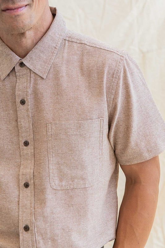 Model wearing Bridge & Burn Malcom short sleeve chambray shirt in rust chambray color, front close up detail view