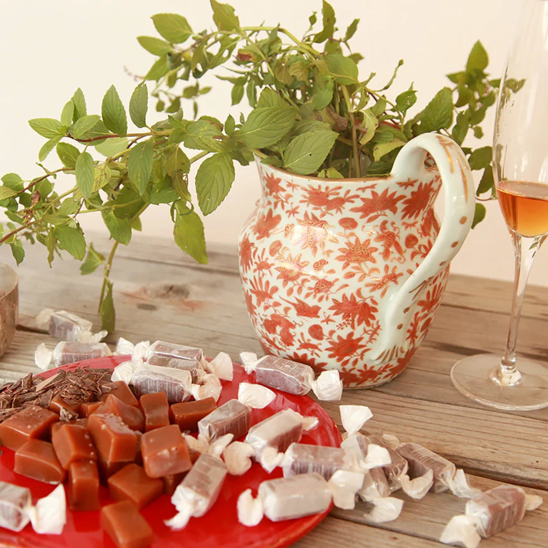 Big Picture Farm goat milk caramels on red plate with wine glass and floral arrangement — assorted Vermont farmstead caramels lifestyle shot
