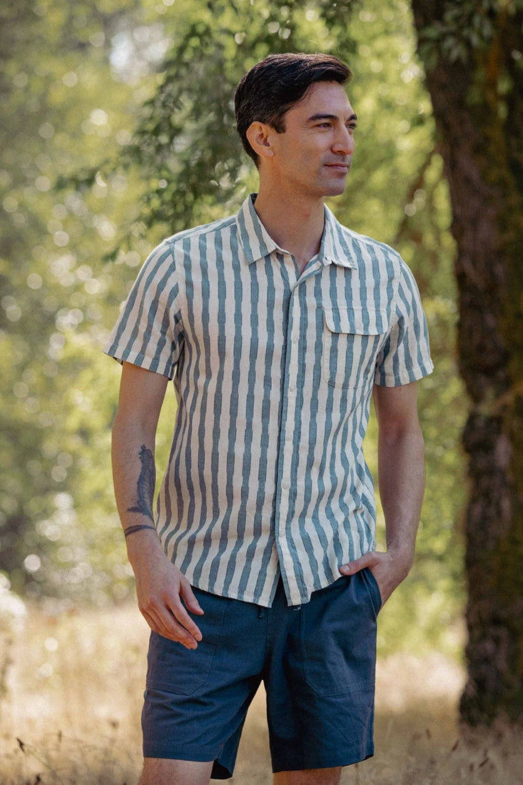 Bridge & Burn Marten Shirt Beach Stripe – front view on model in natural setting wearing men's blue and cream cotton stripe short sleeve shirt