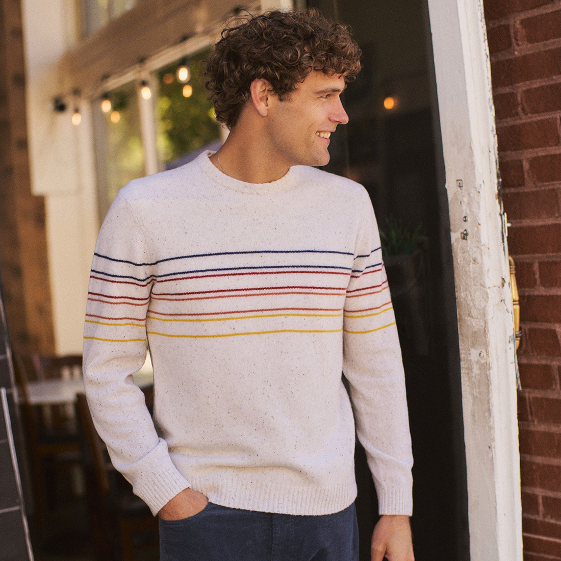 Smiling man in the cream striped merino crewneck standing in a doorway with one hand in his pocket