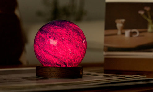 Hand-blown AstraGlass Light showing bright red RGB lighting on its walnut base, styled on a desk with warm ambient décor