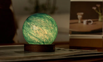 Hand-blown AstraGlass Light in Galaxy Breeze finish glowing green on a walnut wood base, displayed on a tabletop.
