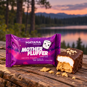 Mother Fluffer mini chocolate bar in its purple wrapper beside a cut piece showing peanut butter and marshmallow, on a wood table by a lake, The Simple Man
