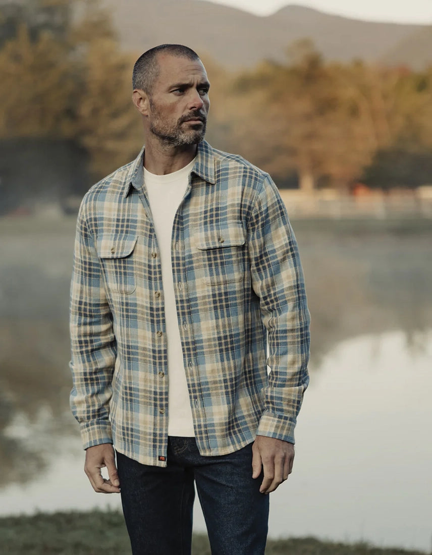 Men’s vintage blue plaid flannel overshirt styled casually with jeans, worn outdoors in a rugged Nebraska landscape—durable cotton shirt from The Simple Man.