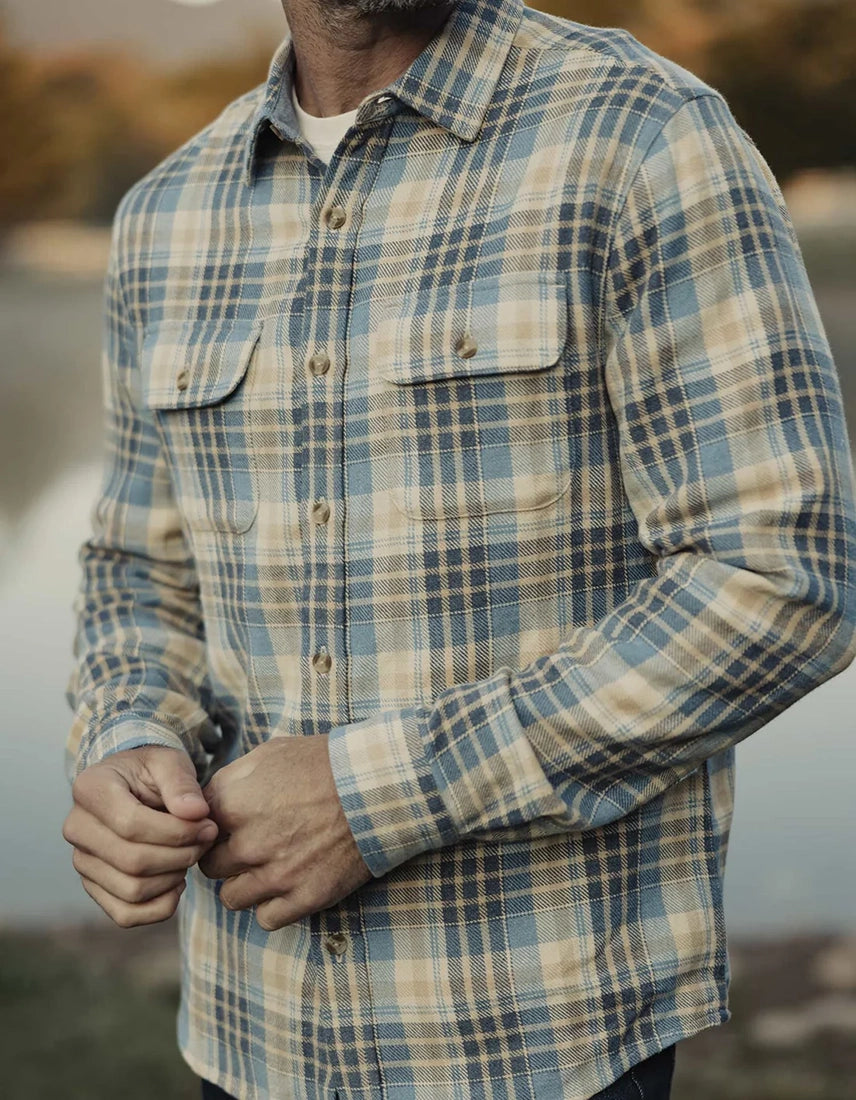 Man wearing vintage blue plaid Mountain Overshirt by The Normal Brand, buttoning front over white tee—heavyweight flannel shirt for men, Omaha lifestyle setting.