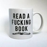 white coffee mug with back text and graphic that reads- Read a Fucking Book