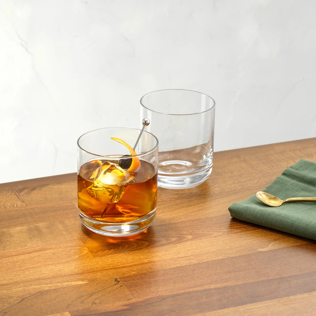 JoyJolt Nova old fashioned whiskey glasses on wood surface – one filled with whiskey cocktail and ice the other empty lead-free crystal 10oz