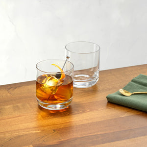 JoyJolt Nova old fashioned whiskey glasses on wood surface – one filled with whiskey cocktail and ice the other empty lead-free crystal 10oz