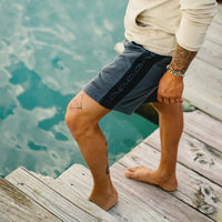 Man wearing Howler Brothers Palmetto Chill Shorts in Washed Navy on wooden dock over turquoise water – men's French terry lounge shorts