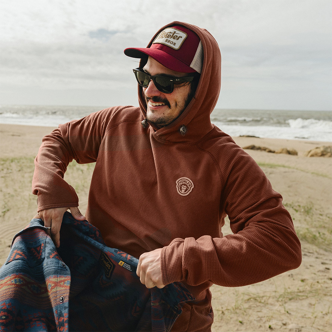 Man wearing the Mink Brown Palo Duro Fleece Hoodie with the hood up on the beach, paired with a Howler trucker hat, The Simple Man