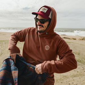 Man wearing the Mink Brown Palo Duro Fleece Hoodie with the hood up on the beach, paired with a Howler trucker hat, The Simple Man