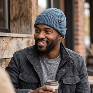 Bearded man smiling in a blue waffle knit Prowl Beanie and charcoal wool jacket, holding a coffee, on model