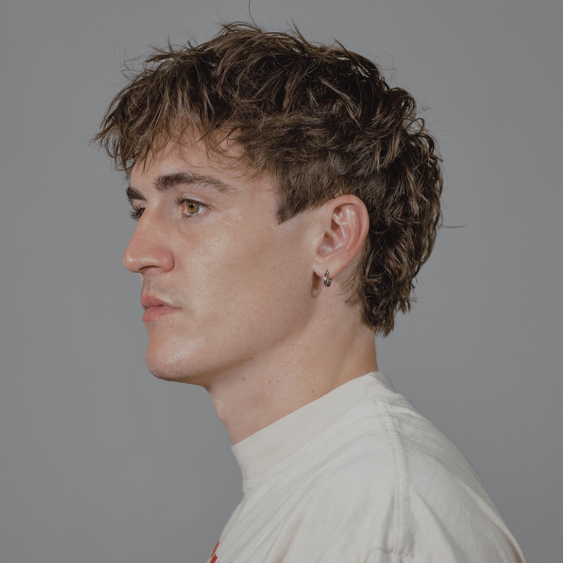 Man in profile with tousled, voluminous curls, styled with Quicksand texture wax