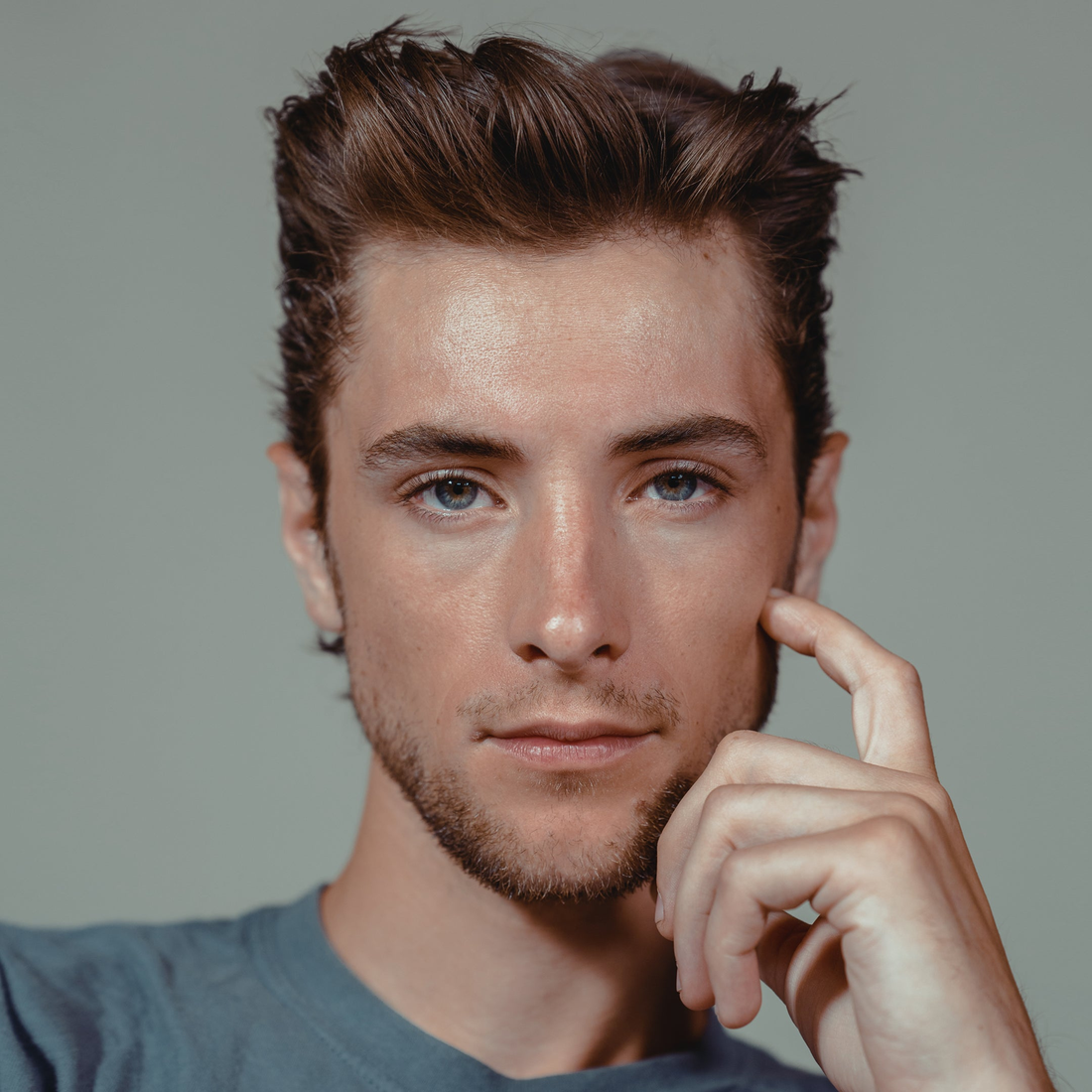 Man with a lifted, textured quiff and a hand at his face, styled with Quicksand