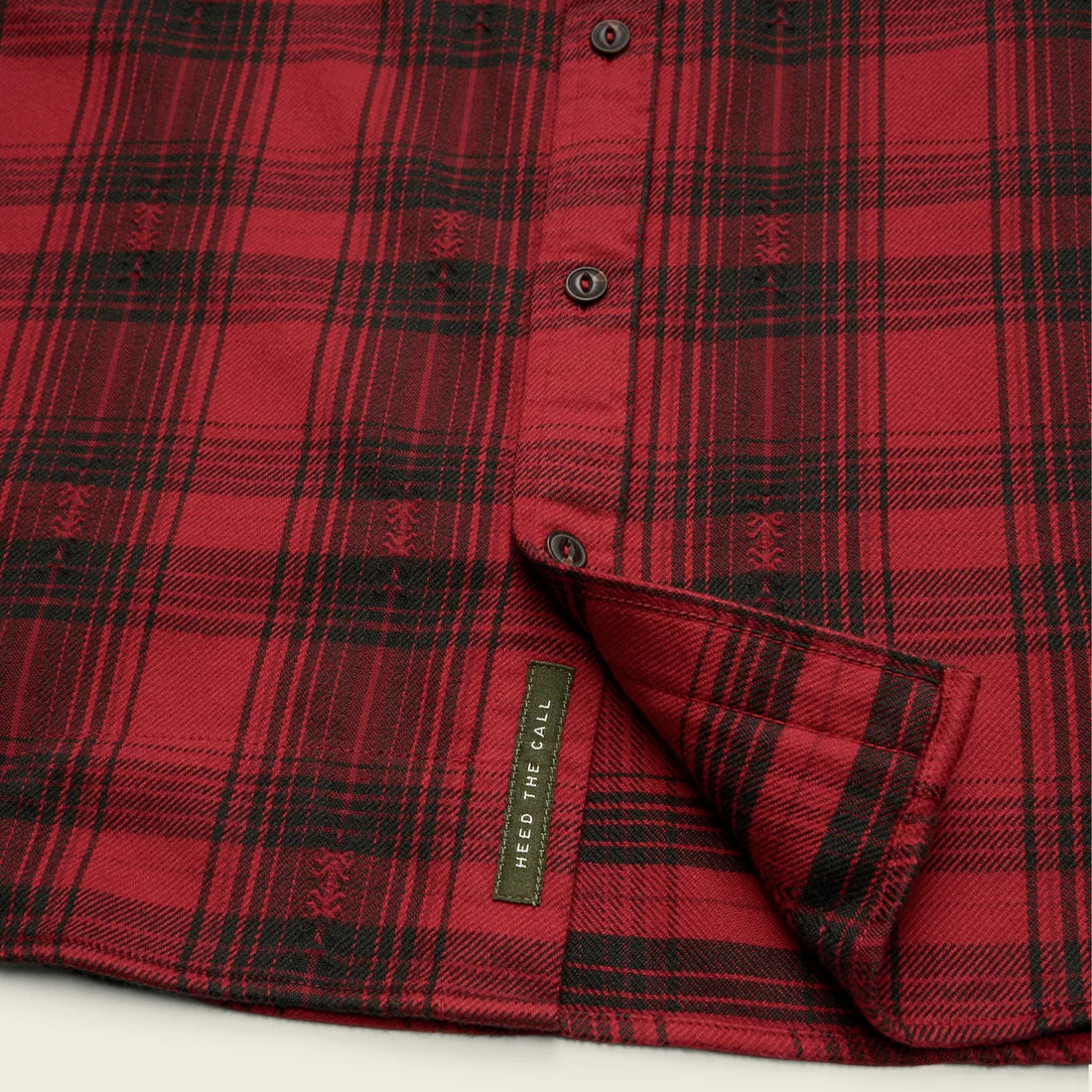 Close-up of Howler Brothers Quintana Flannel – Red and black plaid fabric with ‘Heed the Call’ tag at hem – The Simple Man