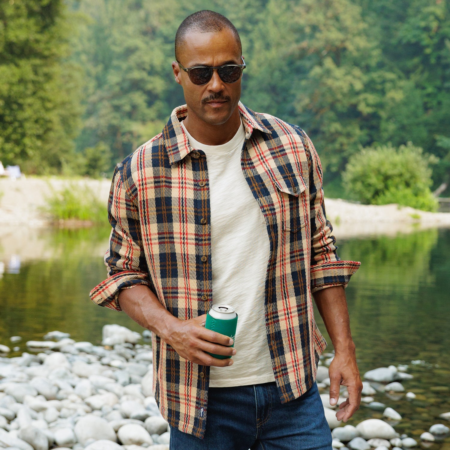 Man wearing Heavy Twill Shacket in Navy Multi Plaid open over a white tee by a river - The Simple Man