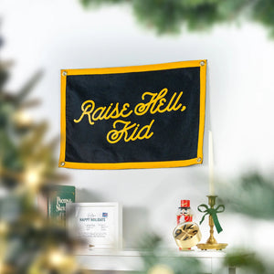 Black and gold Raise Hell Kid mini camp flag hanging above a decorated mantel, lifestyle photo, The Simple Man