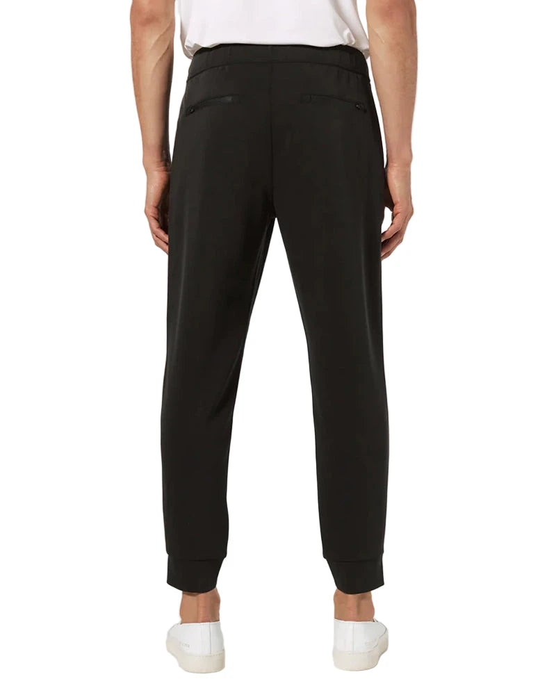 Back view of black REV™ Jogger pants showing tapered fit and hidden zippered pockets, modeled with white tee and sneakers