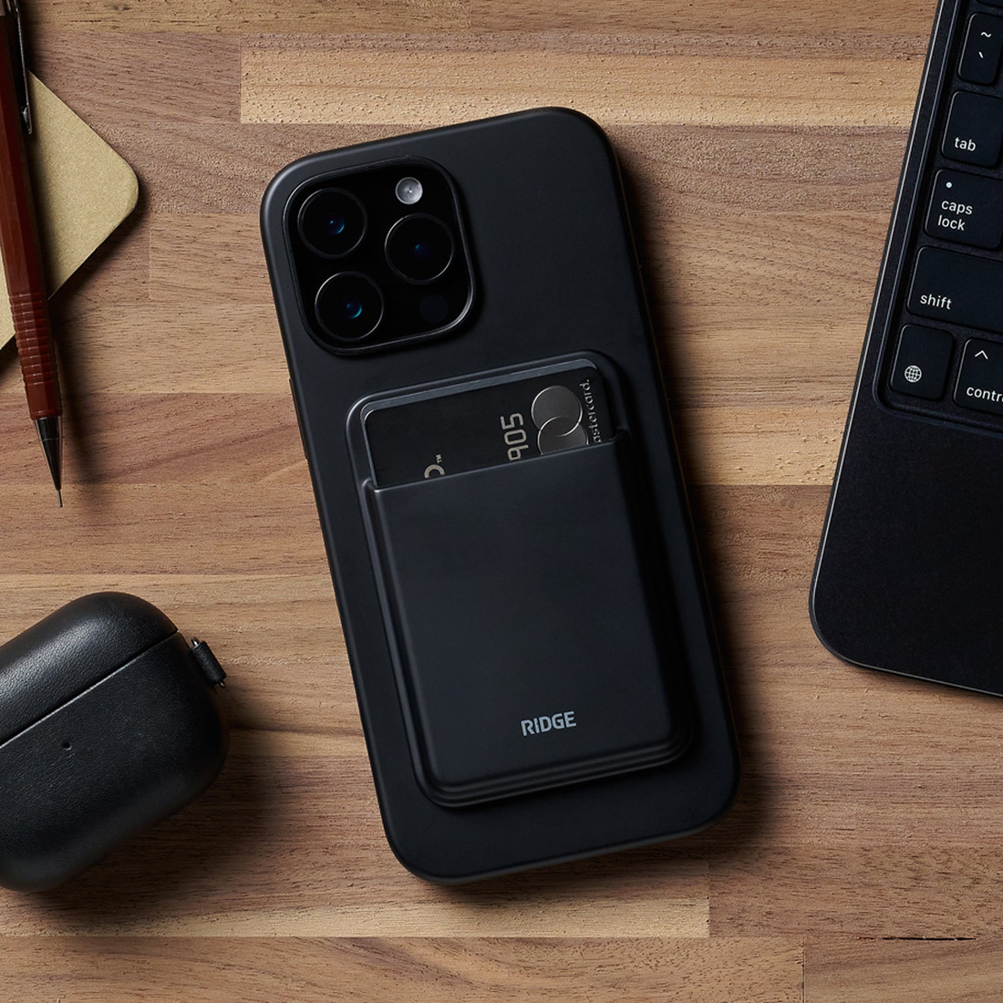 Matte Black cardholder stuck to the back of a phone on a wood desk, two cards peeking out