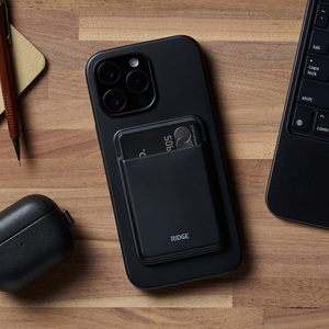 Matte Black cardholder stuck to the back of a phone on a wood desk, two cards peeking out