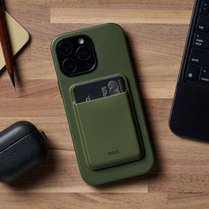 Matte Olive cardholder stuck to the back of a phone on a wood desk, two cards peeking out