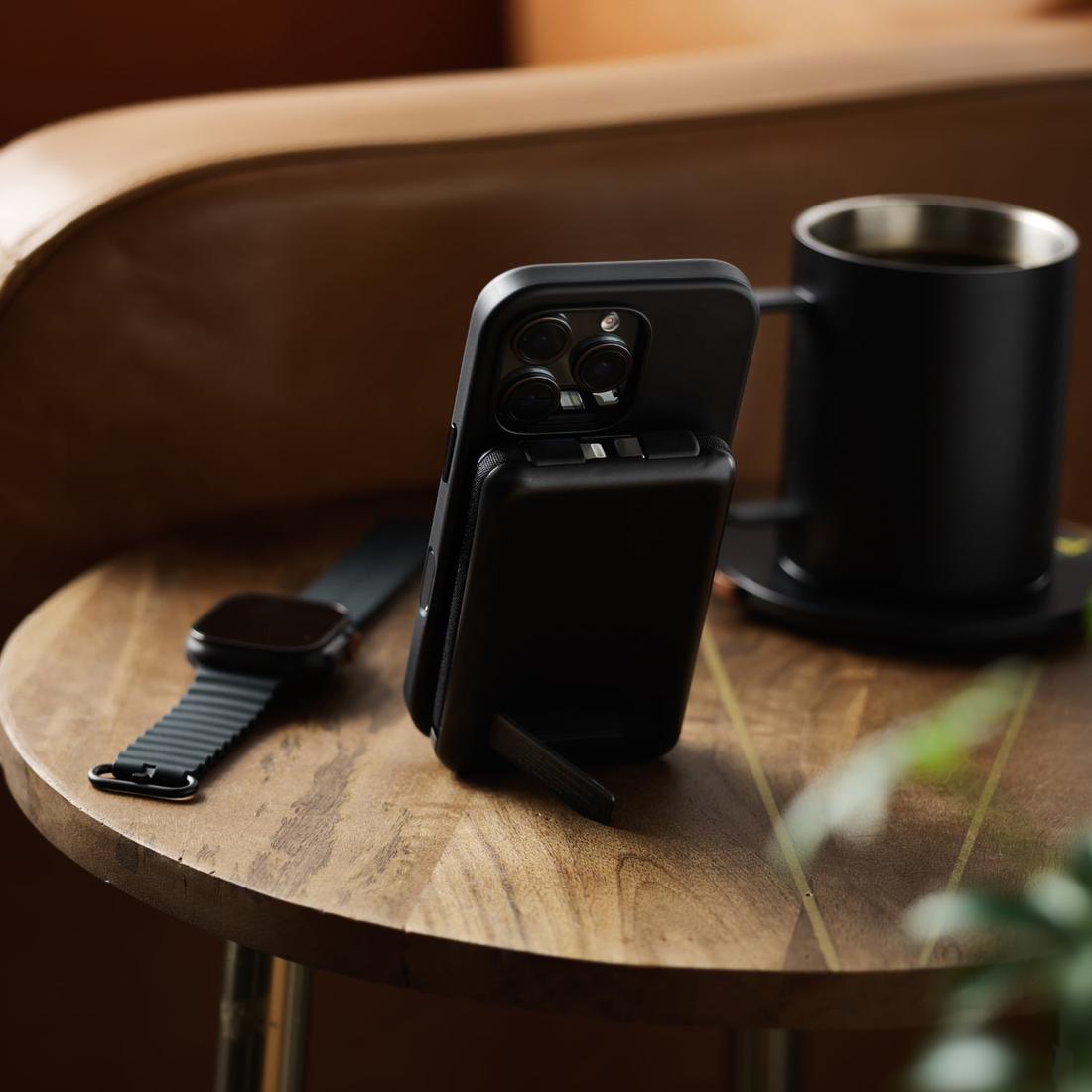 Matte Black power bank on its kickstand holding a phone upright next to a mug and watch