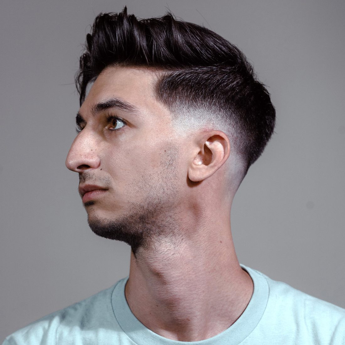 Man in profile with a textured pompadour and tight fade, styled with Scheme Cream