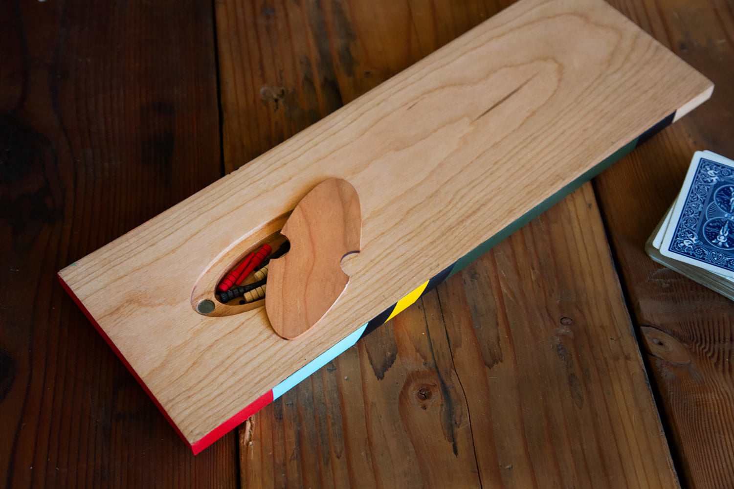 Cherry wood cribbage board with open magnetic storage compartment showing peg set on a wood table.